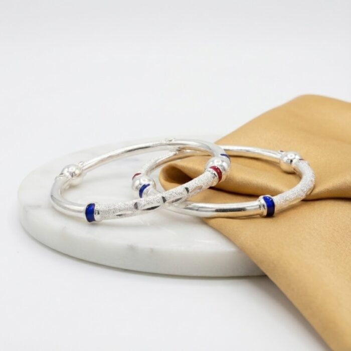 Hollow CNC silver baby bangle with red and blue enamel accents displayed beside concrete block – wholesale silver baby jewellery